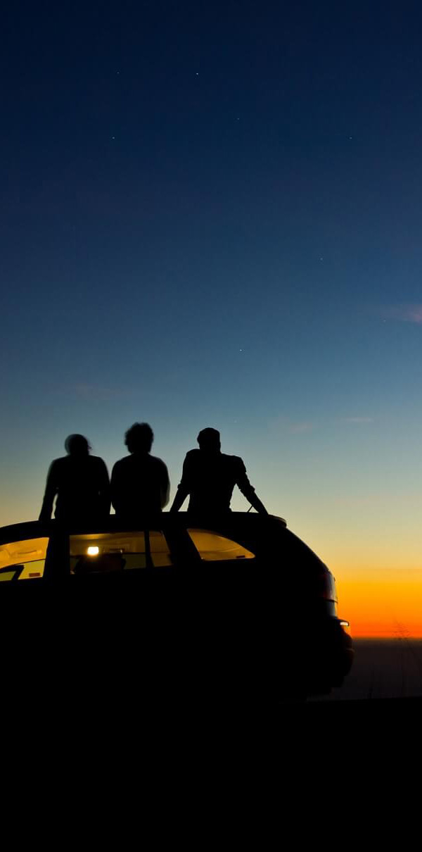 People sitting on car at sunset